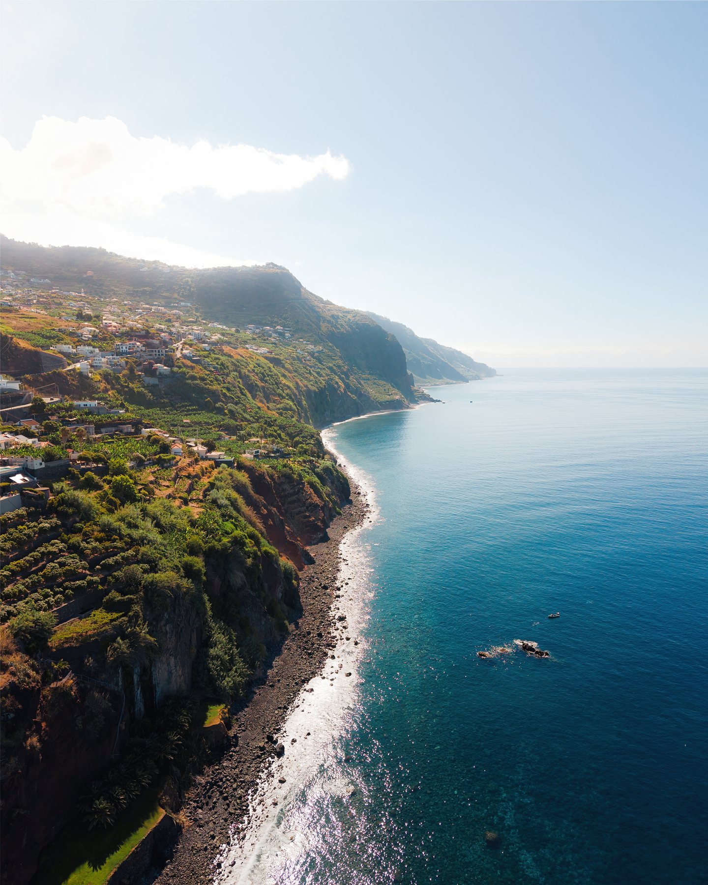 Monument Valley buttes and mesas from Hunts Mesa at golden hour — warm side-light raking across layered red-rock formations, hazy distant spires under a soft clouded sky.